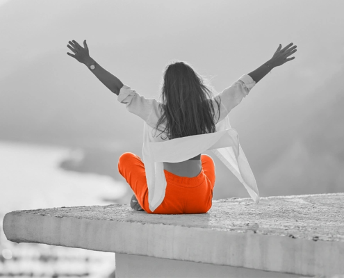 Person sitzt mit erhobenen Armen auf einer Mauer und symbolisiert Selbststeuerung, emotionale Stärke und die bewusste Steuerung des eigenen Zustands.